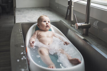 High angle view of cute naked baby boy looking away while lying in bathtub at home - CAVF62916