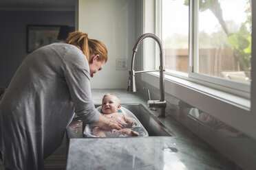 Seitenansicht der Mutter, die ihren niedlichen Sohn in der Küchenspüle zu Hause badet - CAVF62918