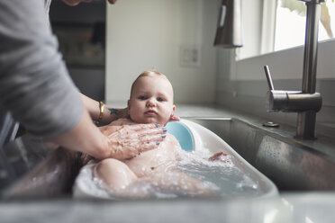 Midsection of mother bathing cute son in baby bathtub at home - CAVF62919