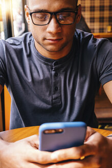 Junger Mann mit Brille benutzt Mobiltelefon in einem Café - CAVF62945