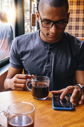 Junger Mann mit schwarzem Kaffee und Smartphone auf dem Tisch in einem Cafe - CAVF62948