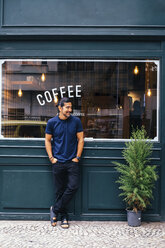 Full length of smiling mature man with hands in pockets standing against coffee shop - CAVF62953