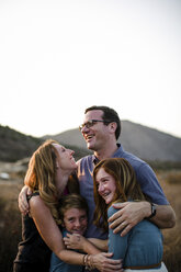 Glückliche liebende Familie, die sich umarmt, während sie gemeinsam auf einem Feld gegen den Himmel bei Sonnenuntergang steht - CAVF62967
