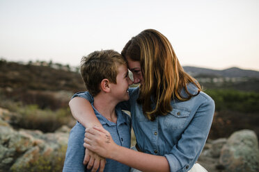 Playful siblings rubbing noses while standing on field during sunset - CAVF62973