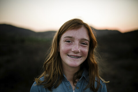 Nahaufnahme eines lächelnden Mädchens mit Zahnspange auf einem Feld vor dem Himmel bei Sonnenuntergang, lizenzfreies Stockfoto