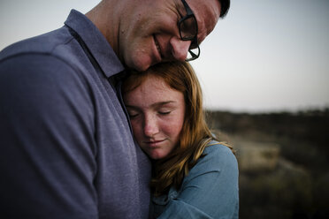Tochter, die ihren Vater umarmt, während sie bei Sonnenuntergang auf einem Feld steht - CAVF62982