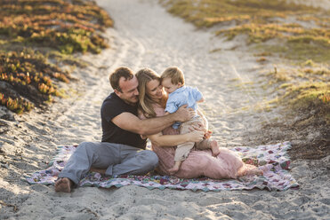 Happy parents talking with son while sitting on sand at beach during sunset - CAVF62987