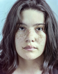 Nahaufnahme Porträt von ernsten Teenager-Mädchen mit Sommersprossen gegen blauen Hintergrund - CAVF62994
