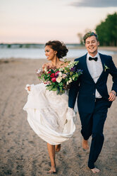 Bride and groom running barefoot on lakeside, Lake Ontario, Toronto, Canada - ISF20959