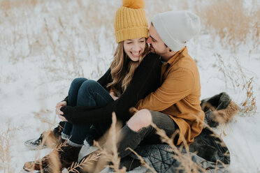 Glückliches Paar auf verschneitem Feld sitzend - ISF20962