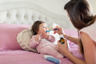 Mother feeding baby girl medicine in bed - ISF20973