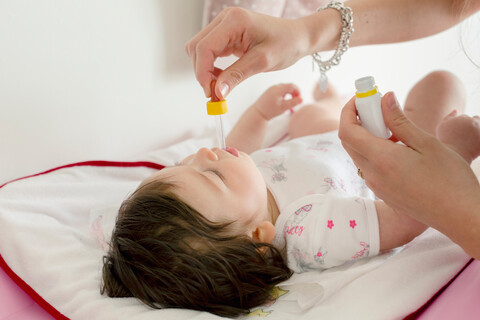 Mutter füttert Baby Mädchen Medizin im Bett, lizenzfreies Stockfoto