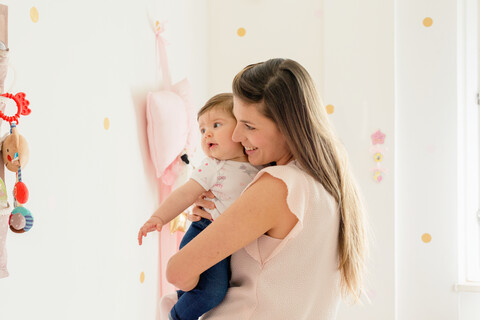 Mutter umarmt kleines Mädchen im Zimmer, lizenzfreies Stockfoto