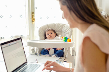 Baby girl watching mother working on laptop at home - ISF20980