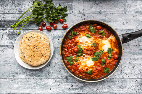 Shakshouka in der Pfanne und Fladenbrot auf dem Teller, lizenzfreies Stockfoto