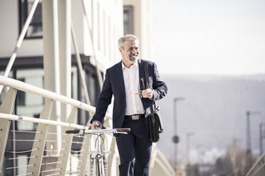 Smiling mature businessman with bicycle in the city - UUF16615