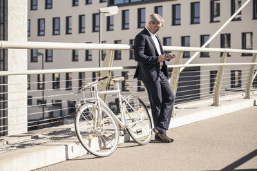 Mature businessman with bicycle using cell phone in the city - UUF16619