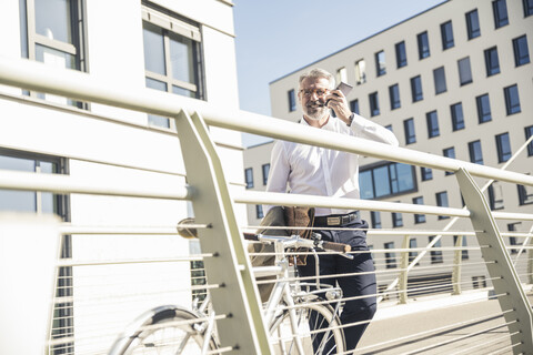 Smiling mature businessman with bicycle using cell phone in the city stock photo