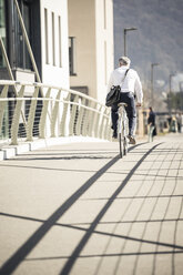 Rear view of mature businessman riding bicycle on a bridge in the city - UUF16632