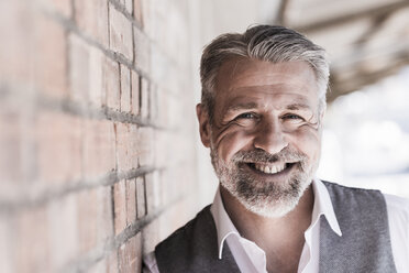 Portrait of smiling mature businessman leaning against a brick wall - UUF16656