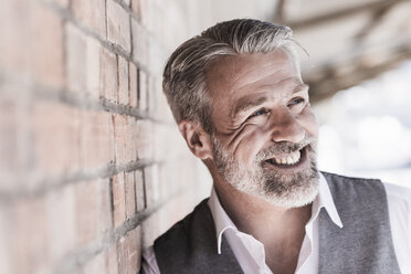 Portrait of smiling mature businessman leaning against a brick wall looking sideways - UUF16657