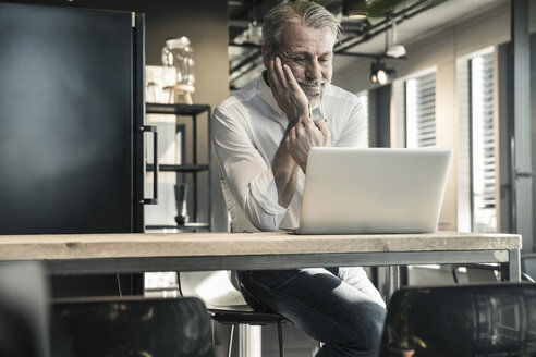 Lächelnder reifer Geschäftsmann mit Blick auf den Laptop im Büro - UUF16679