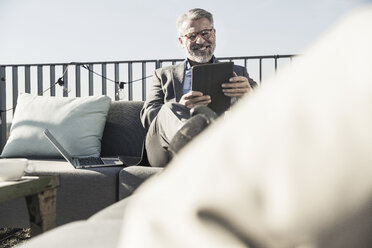 Smiling mature businessman using tablet on roof terrace - UUF16683