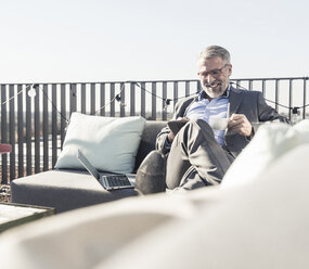 Lächelnder reifer Geschäftsmann mit Tablet auf der Dachterrasse - UUF16685