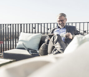 Smiling mature businessman using tablet on roof terrace - UUF16685