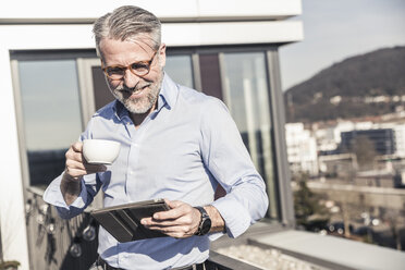 Smiling mature businessman with cup of coffee and tablet on roof terrace - UUF16688