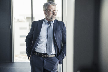 Lächelnder reifer Manager schaut aus dem Fenster im Büro - UUF16694