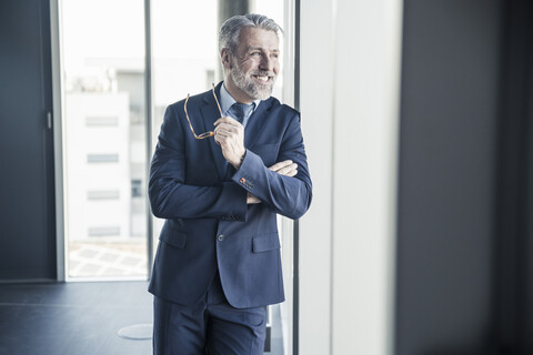 Lächelnder reifer Manager schaut aus dem Fenster im Büro, lizenzfreies Stockfoto