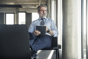 Mature businessman sitting on chair using tablet - UUF16698