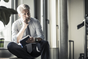 Mature businessman sitting at the window with notebook - UUF16704