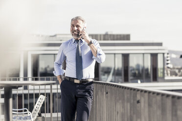 Smiling mature businessman on cell phone on roof terrace - UUF16712