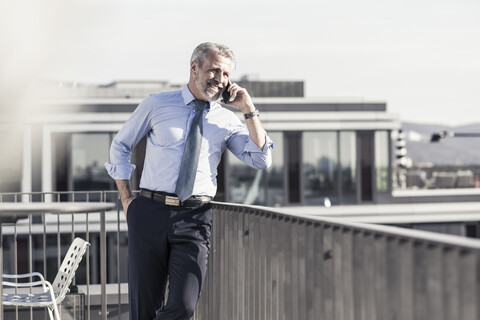 Lächelnder reifer Geschäftsmann am Handy auf der Dachterrasse, lizenzfreies Stockfoto