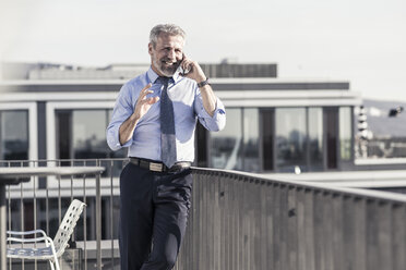 Smiling mature businessman on cell phone on roof terrace - UUF16714