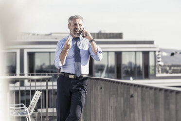 Happy mature businessman on cell phone on roof terrace - UUF16715