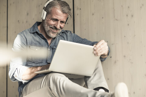 Lässiger reifer Geschäftsmann mit Laptop und Kopfhörern sitzend, lizenzfreies Stockfoto