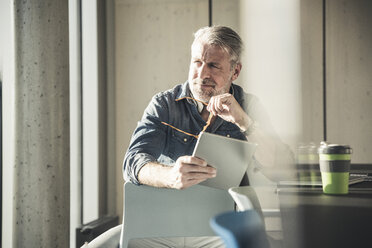 Casual mature businessman sitting at desk with tablet - UUF16731