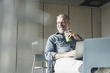 Smiling casual mature businessman with laptop and takeaway coffee - UUF16734