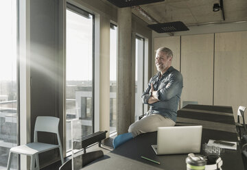 Smiling casual mature businessman looking out of window in office - UUF16742