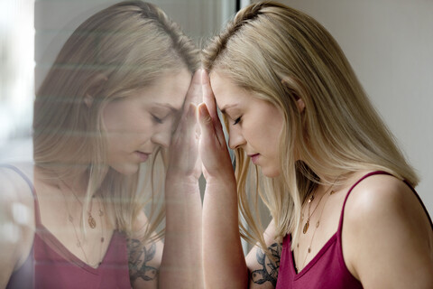 Profil einer blonden jungen Frau und ihr Spiegelbild auf einer Fensterscheibe, lizenzfreies Stockfoto