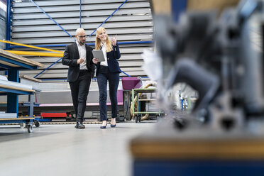 Businessman and businesswoman with tablet walking in factory - DIGF06051