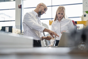 Businessman and businesswoman with laptop examining workpiece in factory - DIGF06059