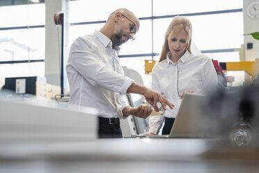 Geschäftsmann und Geschäftsfrau mit Laptop bei der Prüfung eines Werkstücks in einer Fabrik - DIGF06059