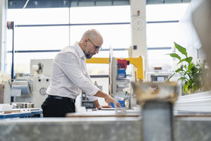 Fokussierter Geschäftsmann, der ein Werkstück in der Fabrik untersucht - DIGF06068