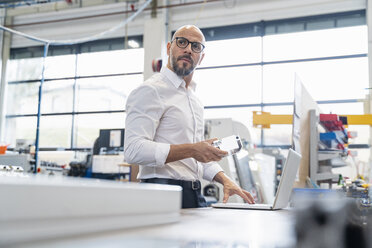 Businessman with laptop holding workpiece in factory - DIGF06069