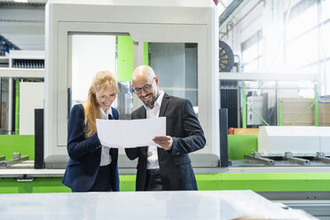 Smiling businessman and businesswoman looking at plan in factory - DIGF06073