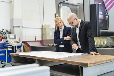 Businessman and businesswoman looking at plan on table in factory - DIGF06086